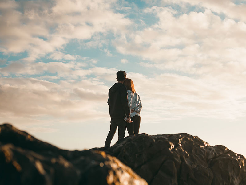A couple who knows the difference between a healthy vs. unhealthy fights standing on a mountain looking at the sky.