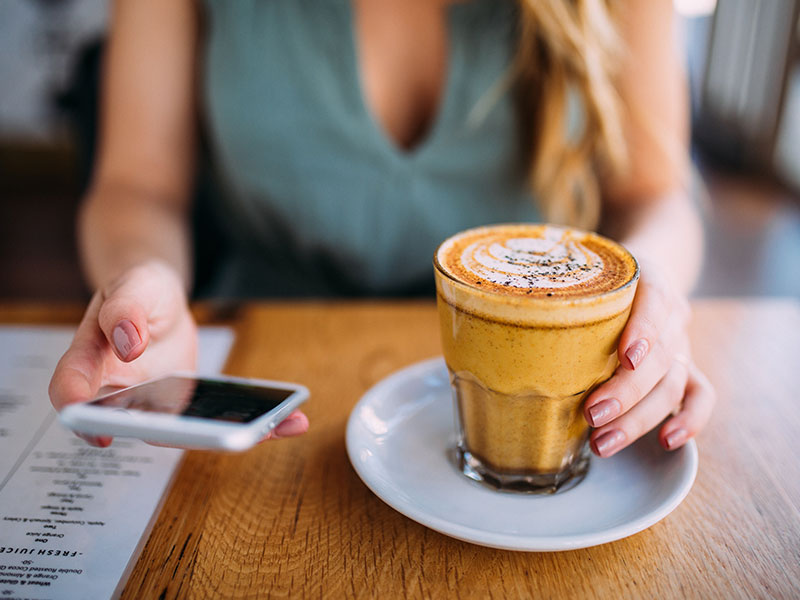 A woman who took these online dating tips for women to write a good message on her phone while drinking coffee.