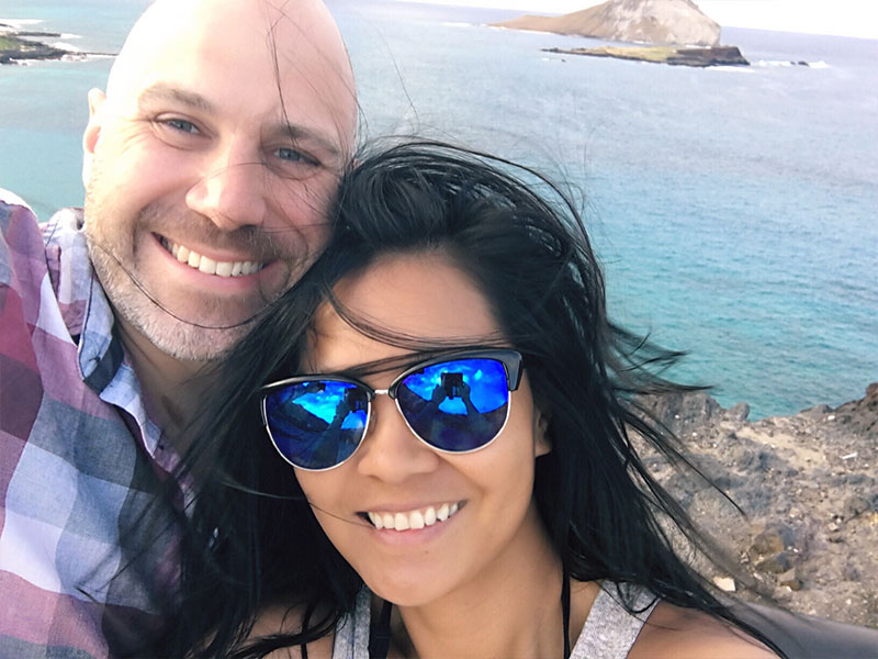A man who knows older men dating younger women is a gender norm, smiling with his younger girlfriend on the beach.