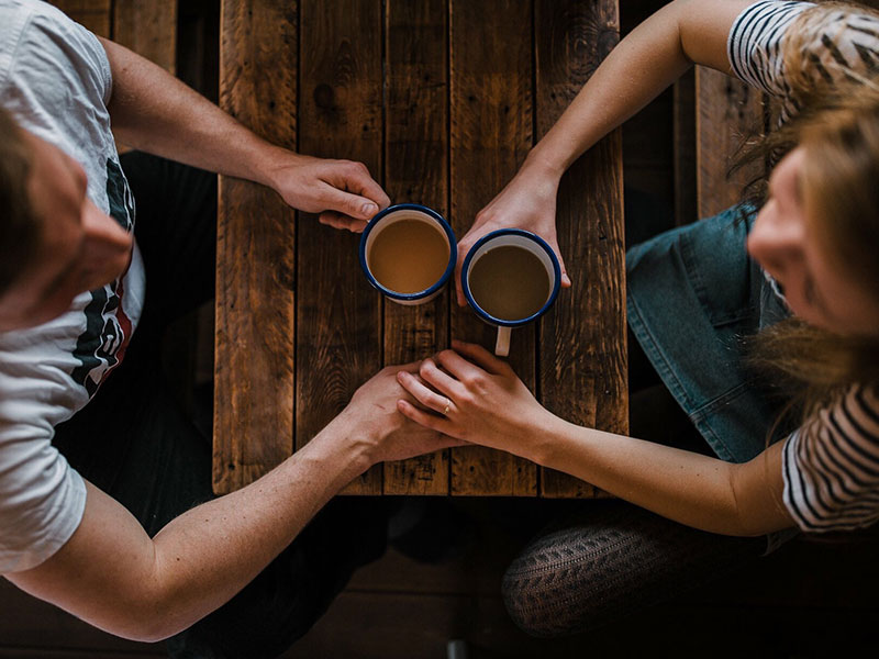 Two singles over 40 holding hands while on a date at a coffee shop.