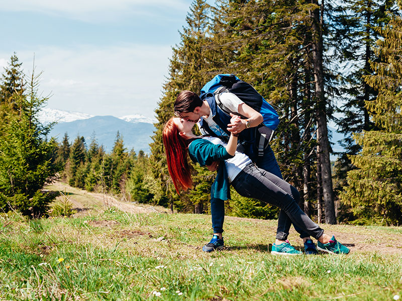A couple kissing in the woods while on a hike.