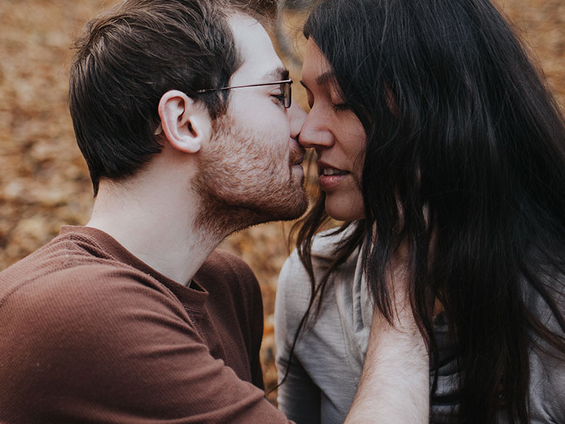 A woman thinking about getting back with an ex, closing her eyes while she kisses her ex boyfriend.