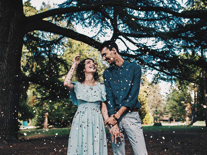 A woman who learned how men fall in love, smiling with her husband under a tree at their wedding.