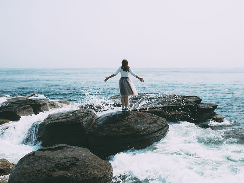 A woman who used this break up survival kit standing on a rock in front of the ocean feeling powerful.