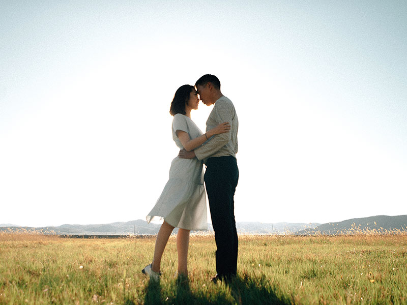 A couple who practices self-care hugging in a field.