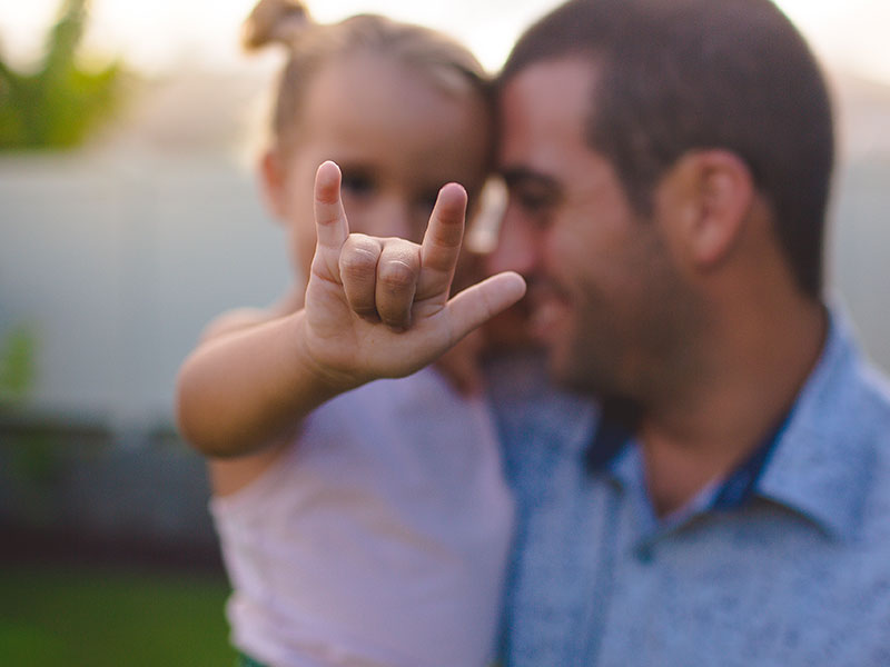 A single dad dating, holding his daughter and laughing as she gives the rock on symbol with her hand.