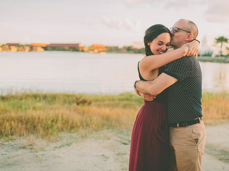 A younger woman dating an older man giving him a hug by a lake.