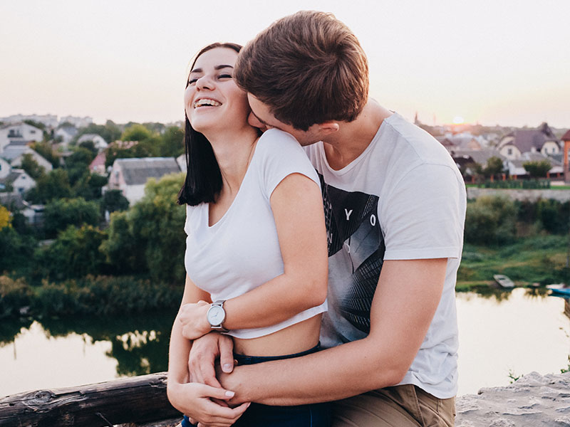 A couple who read these dating advice articles laughing and smiling as they hug at sunset.