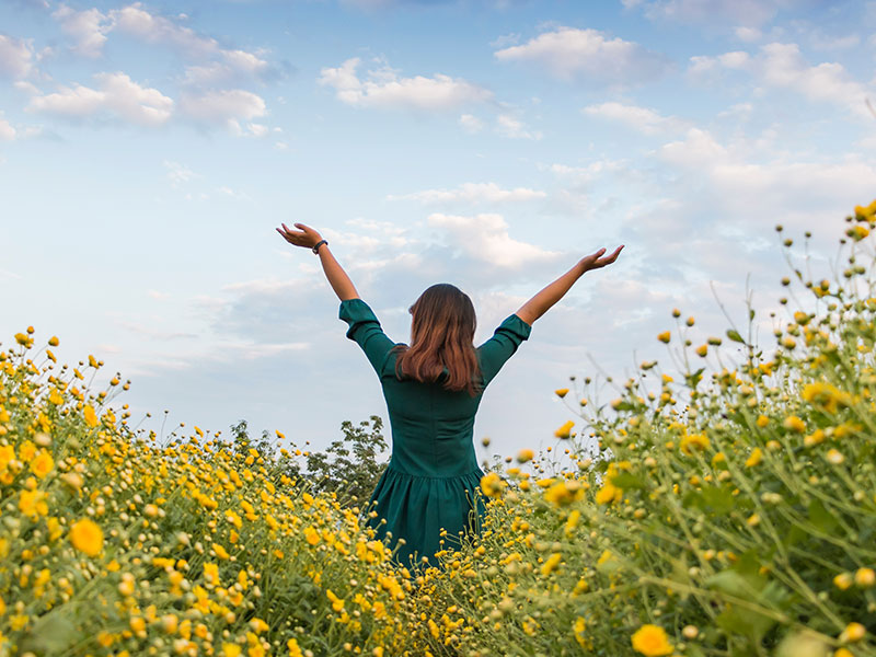 A woman who took these moving forward quotes to heart standing in a field of flowers with her arms raised towards the sky.
