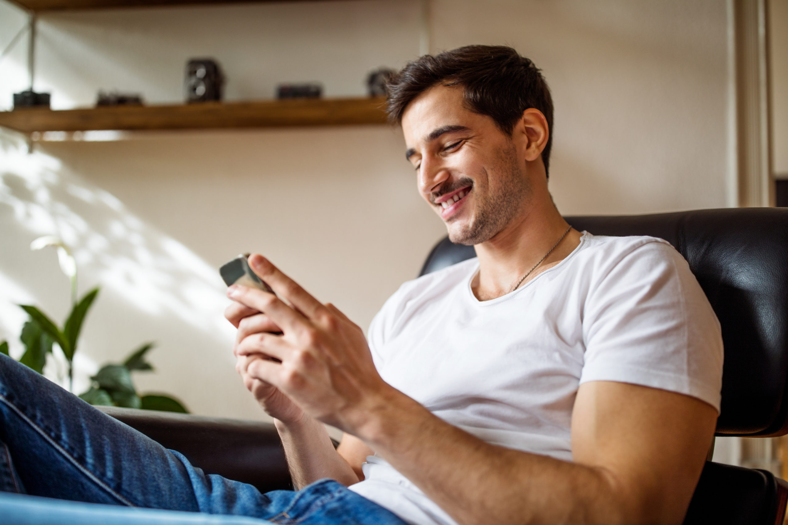 Young man using smartphone for online dating and choosing between Bumble vs. Tinder.