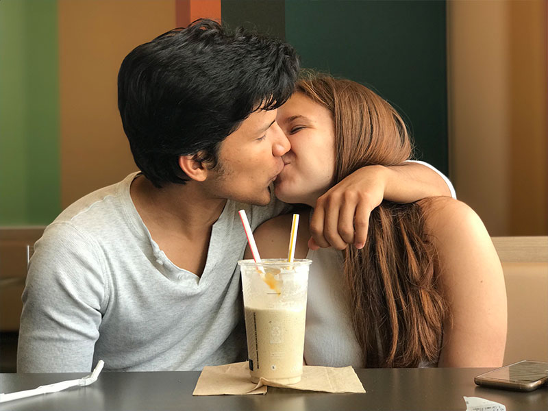 A women who listened to some of the best dating advice for women, kissing her boyfriend on a date with the milkshake they’re sharing in front of her.