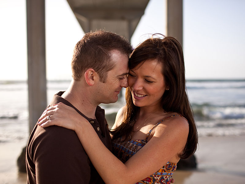 A couple dating after divorce with kids, hugging and laughing under a pier on the beach.