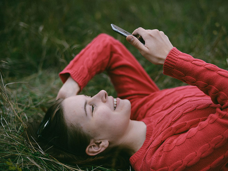A woman in the grass looking at a dating app on her phone, using some of these digital dating tips.