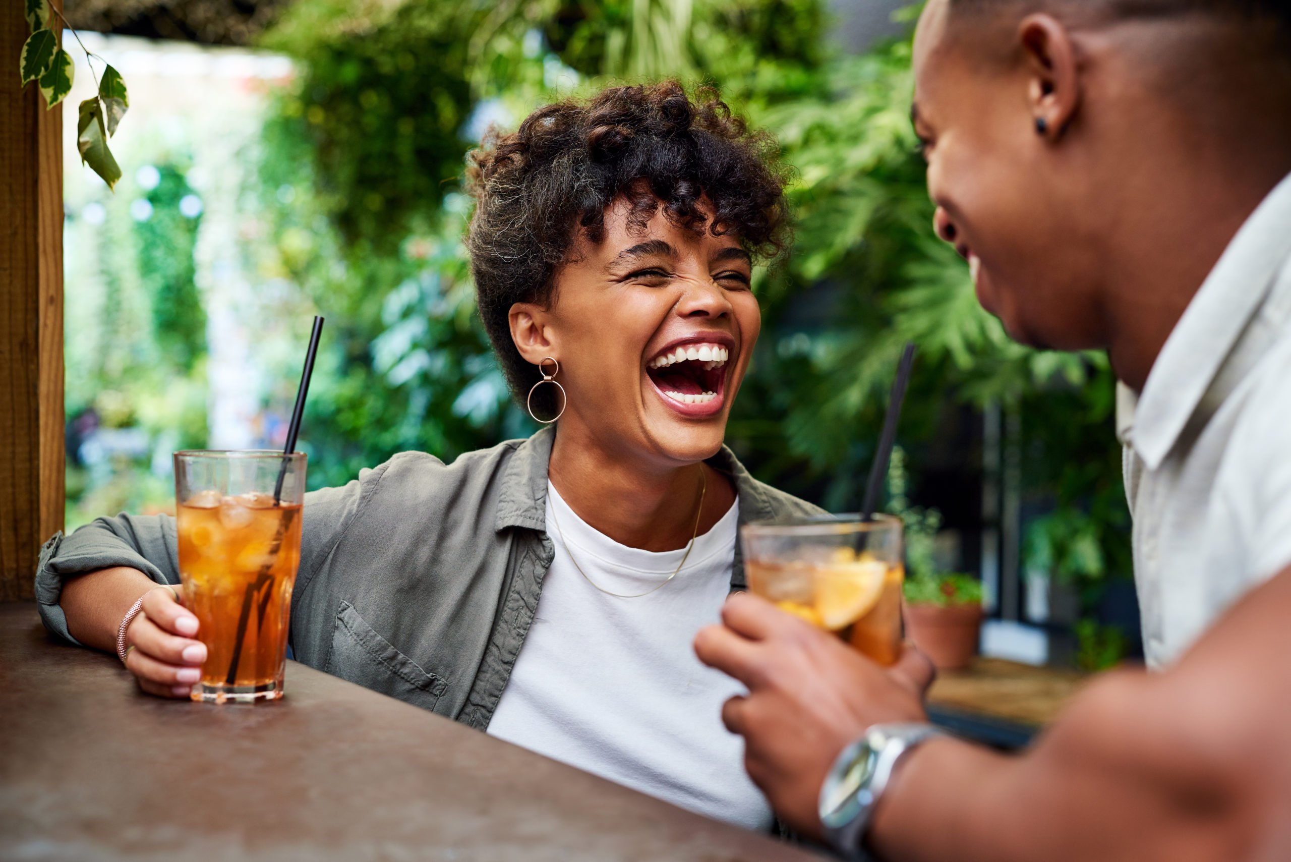 Happy couple sitting in an outdoor bar and laughing together while enjoying a good second date idea.