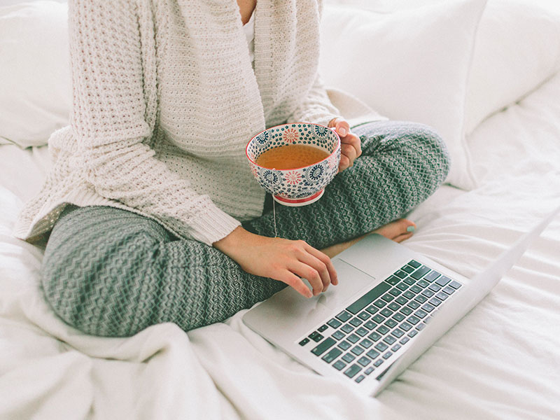 A woman using these dating profile tips to update her online dating profile while she's in bed drinking coffee.