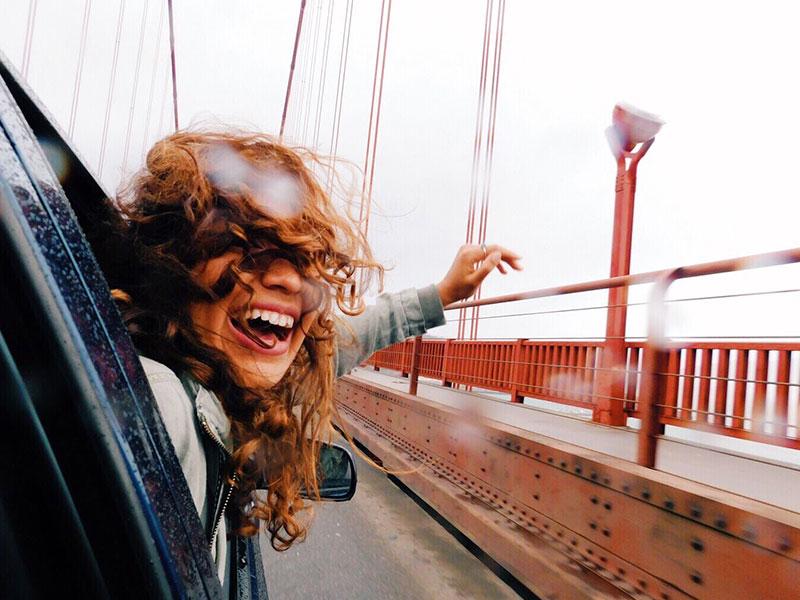 A woman who's letting go of someone, hanging out a car door window with a smile as she goes over a bridge and moves on with her life.