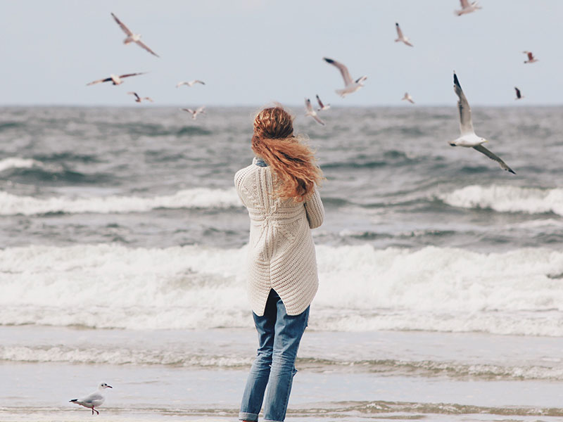 A woman who's wondering why her boyfriend is acting weird, standing on the beach alone and wondering.