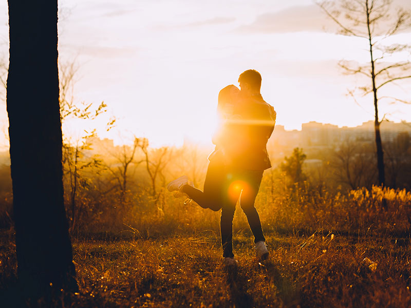 A man who learned when to say I love you, spinning his girlfriend around in a field at sunset.