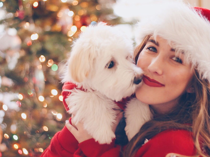 A woman in her 40s, hugging her dog in front of her Christmas tree.