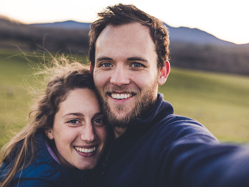 A couple who met on one of the best Christian dating sites, smiling as they take a selfie together in front of a mountain.