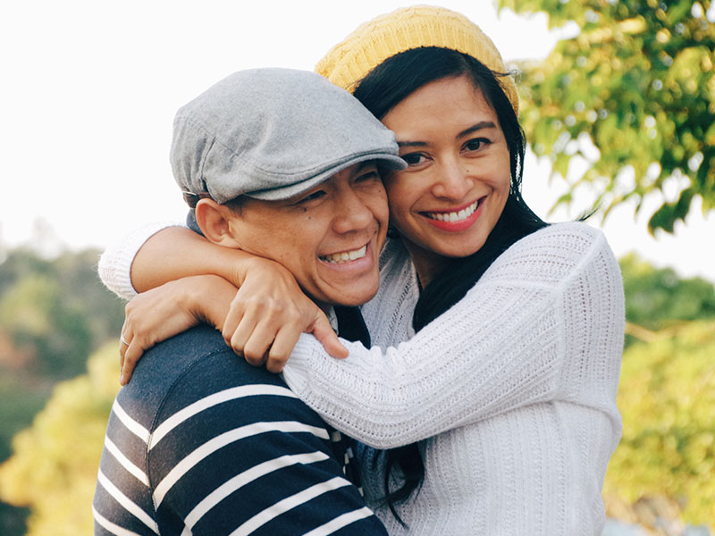 Two friends in a flirtationship hugging and laughing as they flirty at a party.