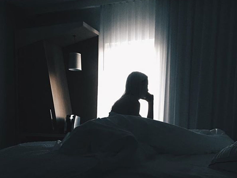 A woman who learned what is pistanthrophobia, sitting in her bed alone thinking about the phobia.