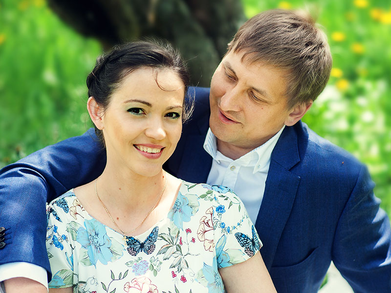 A woman who knows what it's like dating in your 30s, smiling in the grass as her boyfriend sits with his arm over her.