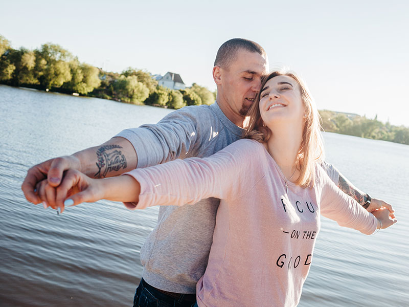 A couple who are dating their best friends, hugging and laughing in front of a lake.