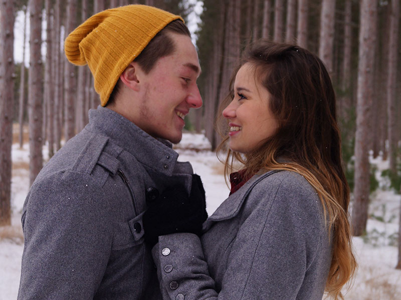 A guy who said I want a relationship, looking into his girldfriend's eyes and smiling while they stand in the woods in the snow.