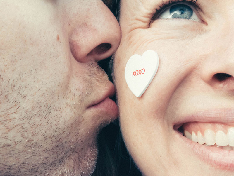 A couple that met on over 50 dating sites, smiling as the man kisses the woman's cheek.