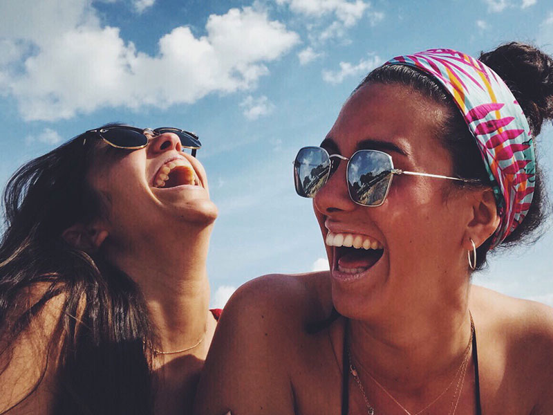 Two women who show these qualities of a good friend, laughing together outside in the sun.