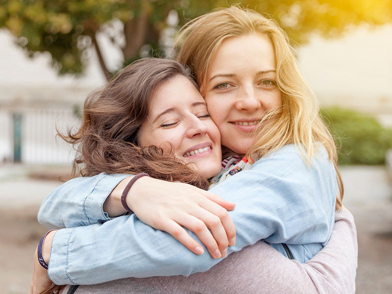 A girl who knew what to say to a friend after a breakup hugging her friend as she smiles and hugs back.