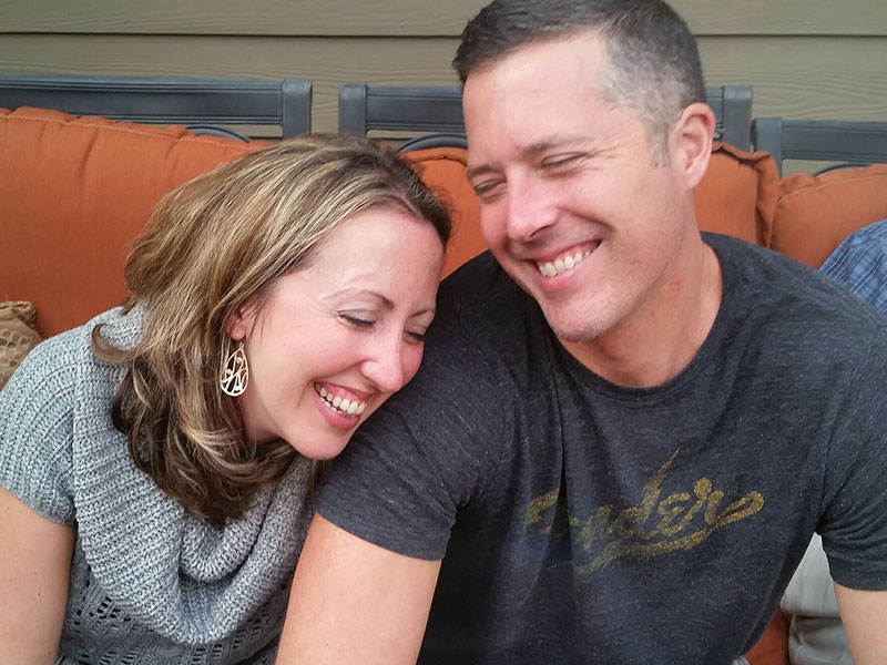 A couple dating after 40 smiling and laughing together outside at a BBQ.