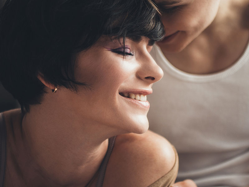 A woman who listened to these dating tips or women, smiling as her boyfriend cuddles her neck.