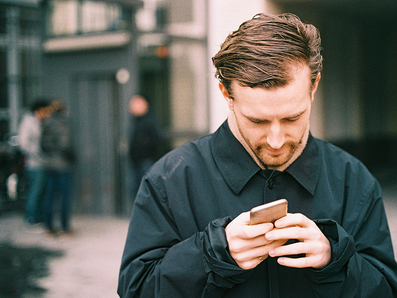A guy looking through fake Tinder profiles while outside looking confused.