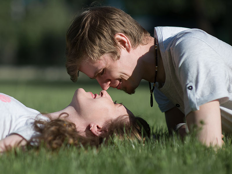 A woman wondering how to attract men, lying in the grass and looking up into the eyes of man flirting with her.