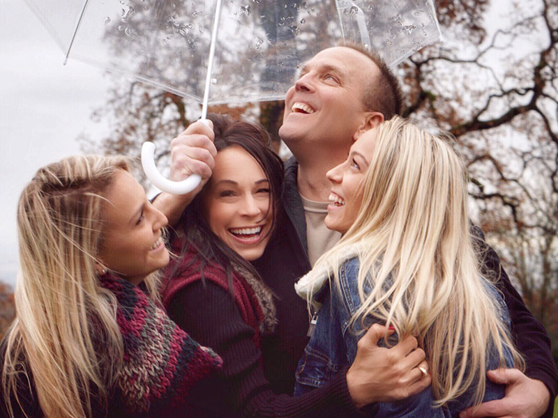 A group of people hugging and laughing under an umbrella showing some of these 3 types of love.