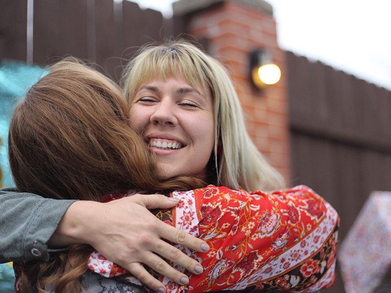 Two friends that know that friends come and go, hugging and laughing as they greet each other.
