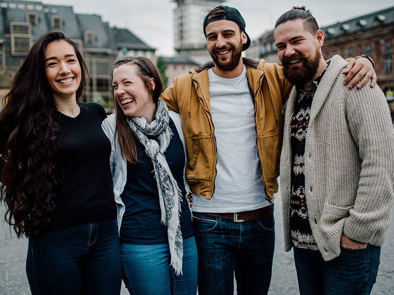 A group of men and women who learned how to make friends in a new city, hugging and laughing with each other as they hang out.