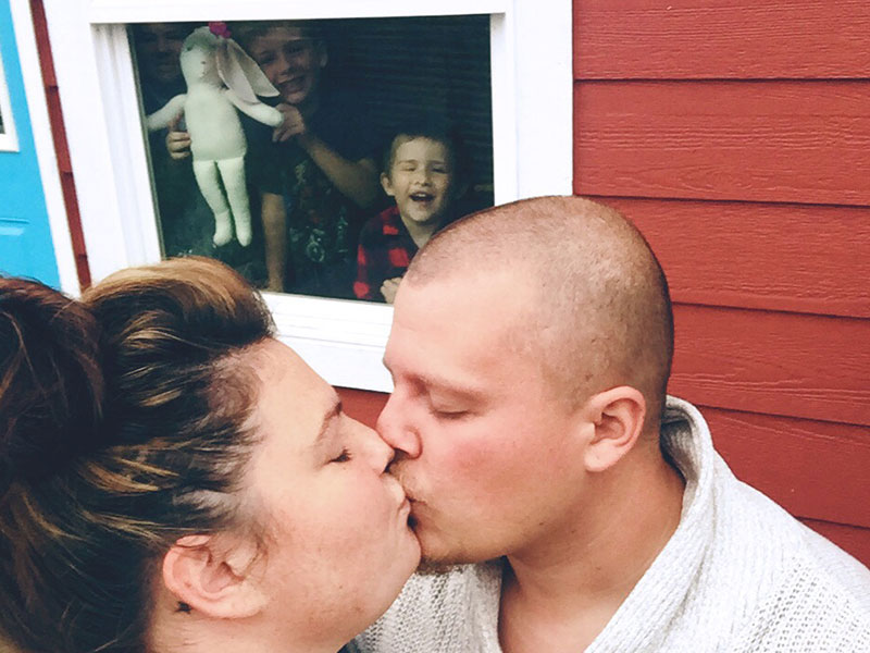 A woman who's a single parent and dating, kissing her date while her kids are inside pushing their faces against the window and making funny faces.
