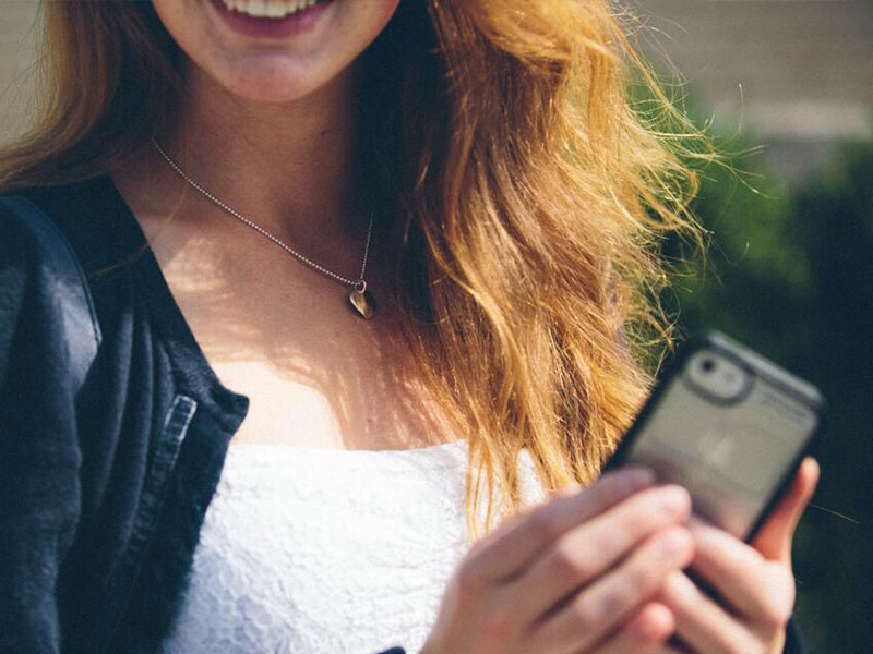 A woman who's trying to avoid text flirting mistakes, laughing while outside on her phone typing.