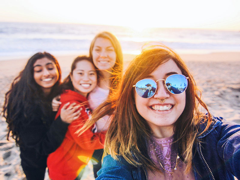 A group of girls who met on a Tinder for friends app, at the beach smiling as they take a picture.