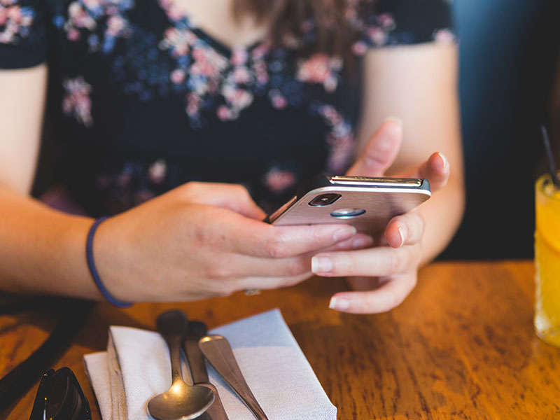 A woman who took these dating profile tips, at a restaurant looking through dating profiles on her phone.