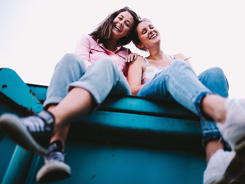 Two friends hanging out and smiling while sitting together outside.