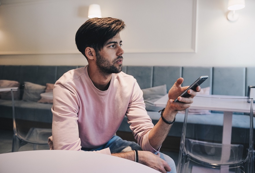 attractive young man on his mobile phone in a coffee shop thinking about how often to text a girl