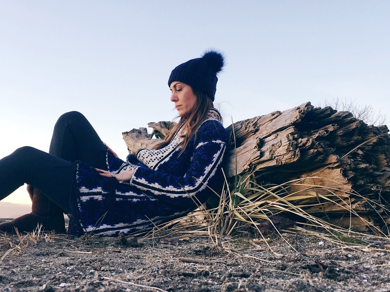 Sad looking woman sitting on the ground, leaning against a rock and thinking about the signs your marriage is over