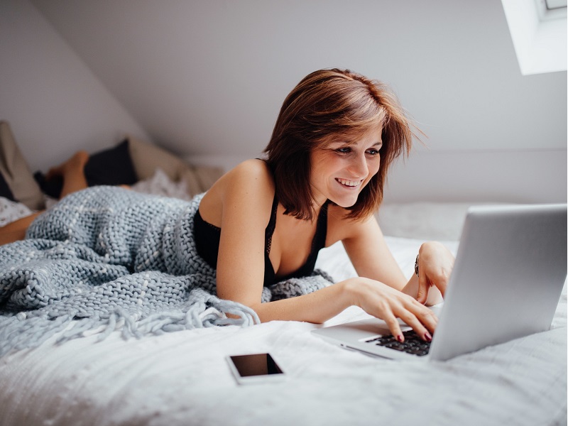 attractive lady lying in bed and using online dating profile templates to set up profile