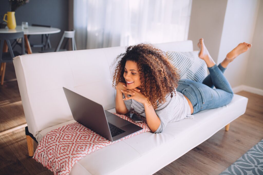 Woman lying down on sofa, smiling and making connections on a black dating site.