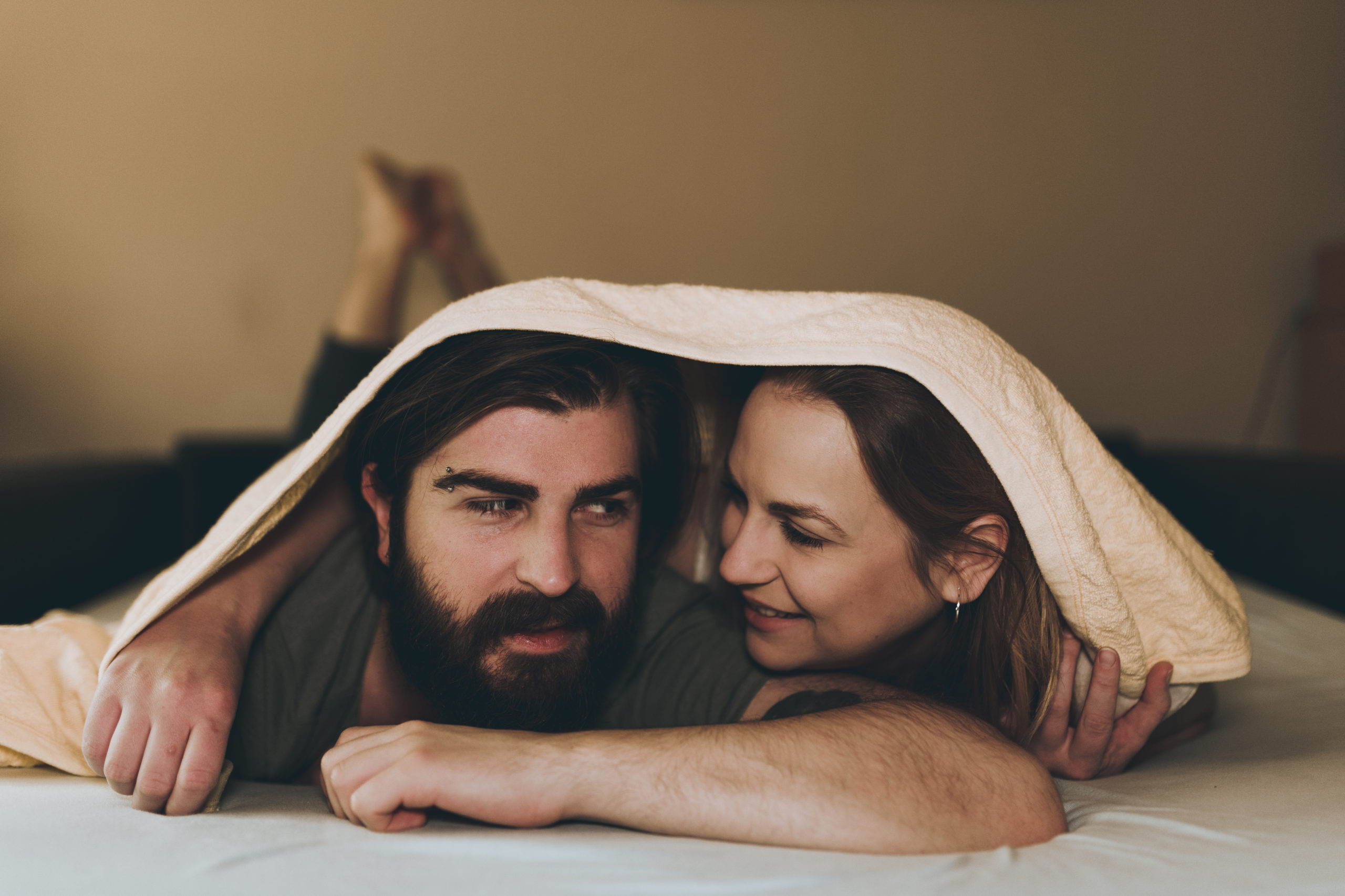 Couple in a just sex relationship lying in bed under duvet and smiling at each other.