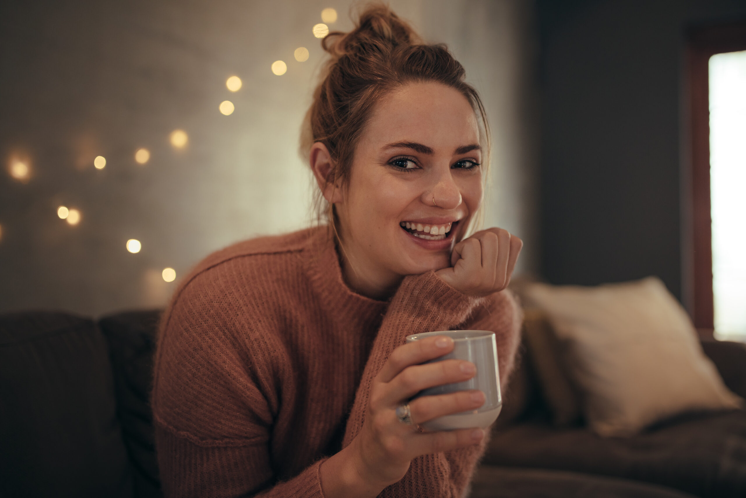 Happy woman sitting on a sofa, looking towards camera and smiling as she discovers that self love is the best love.